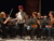 junger Schauspieler verteilt Papiere an Orchestermusiker:innen