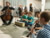 Kinder und ein Cellist musizieren im Vordergrund, Orchestermusiker:innen stehen im Hintergrund