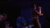Konzertraum in blau beleuchtet, ein Sänger steht im Zentrum, daneben eine Person am Mischpult.