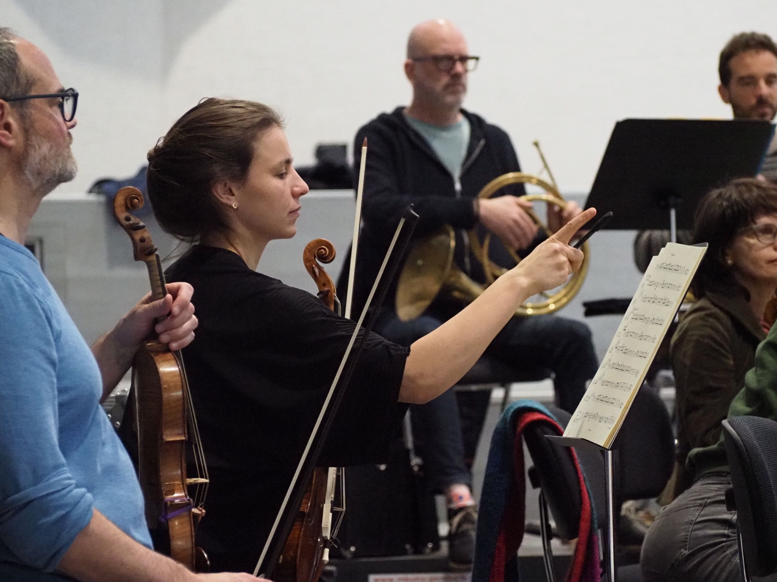 Geiger:innen in der Orchesterprobe, zeigt mit dem Finger nach vorne.