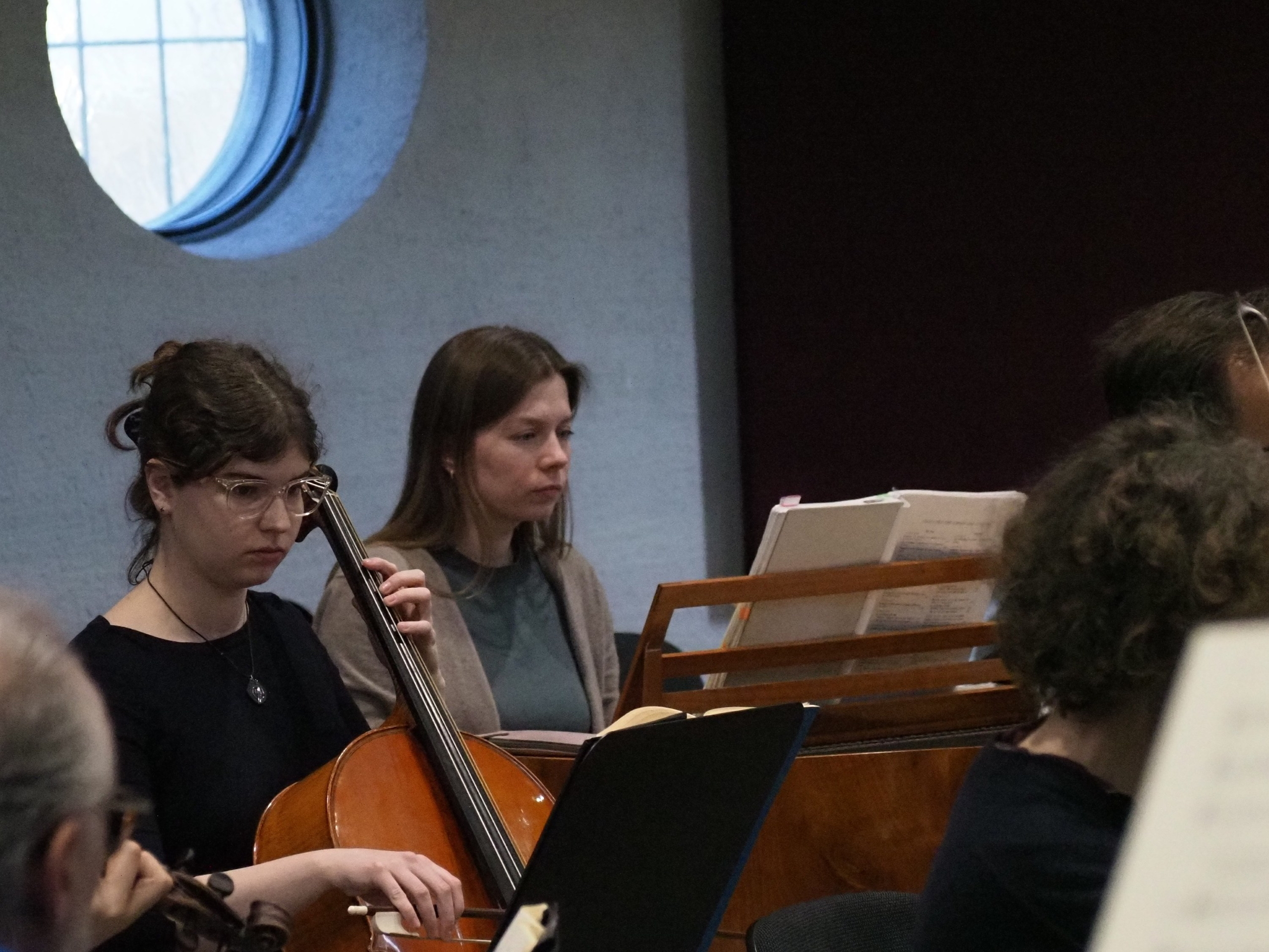 Cellistin sitzend in der Orchesterprobe, neben dem Cembalo