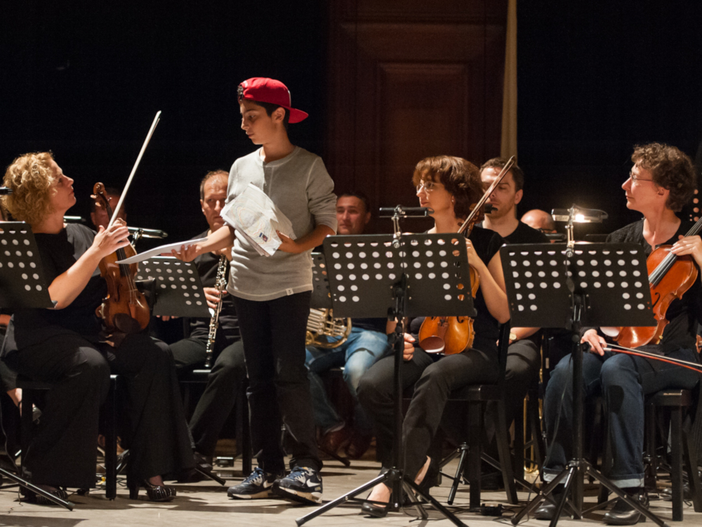 junger Schauspieler verteilt Papiere an Orchestermusiker:innen