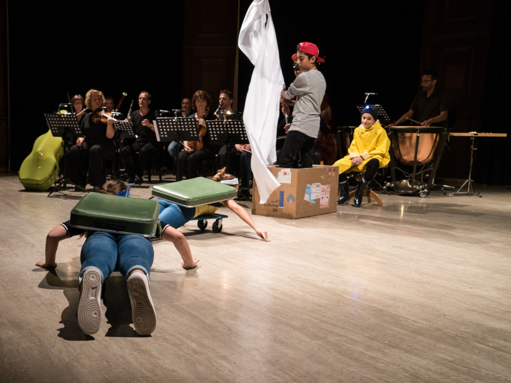 junge Schauspieler:innen im Vordergrund, Orchester im Hintergrund