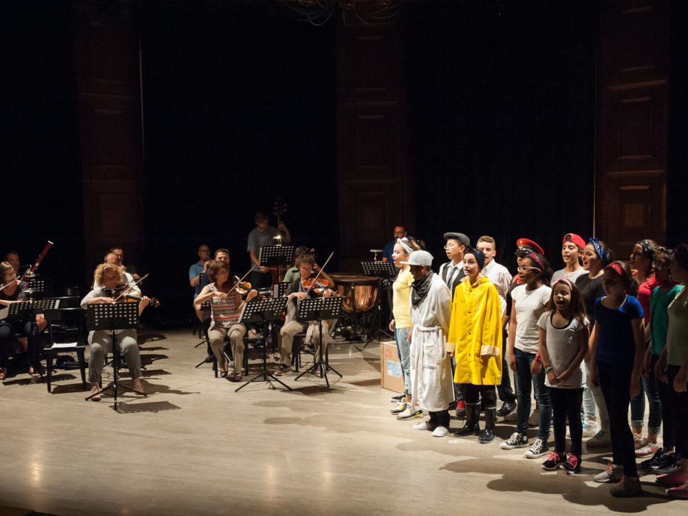 Kinder singen im Chor, daneben spielt das Orchester