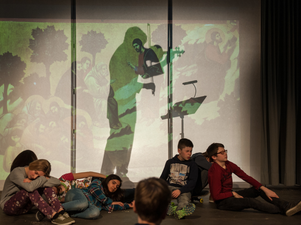 Geiger spielt hinter Schattenwand, junge Darsteller:innen stellen sich davor schlafend