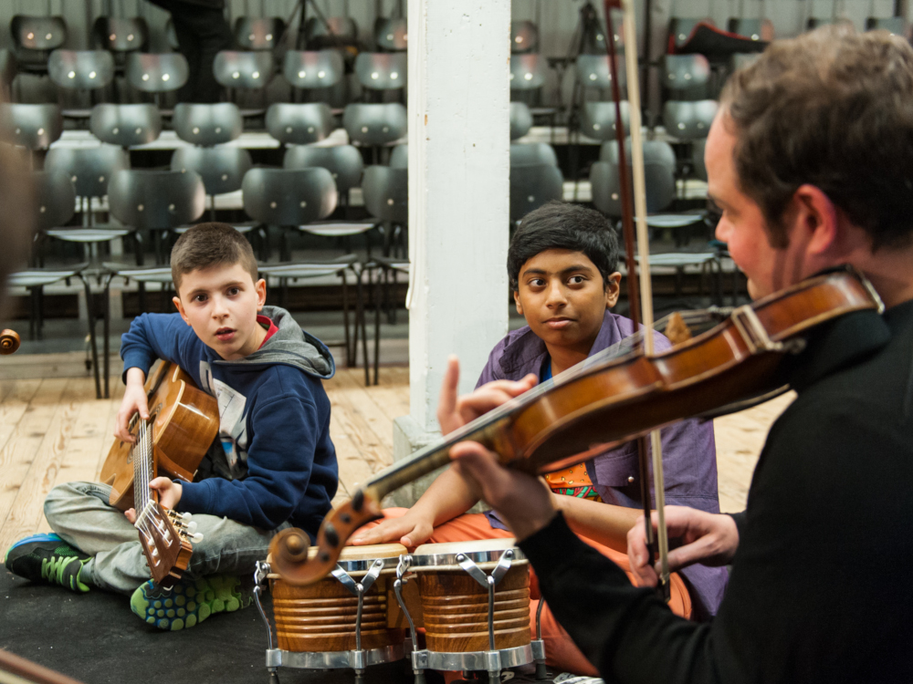 zwei Jungs spielen Gitarre und Bongos gemeinsam mit einem Geiger