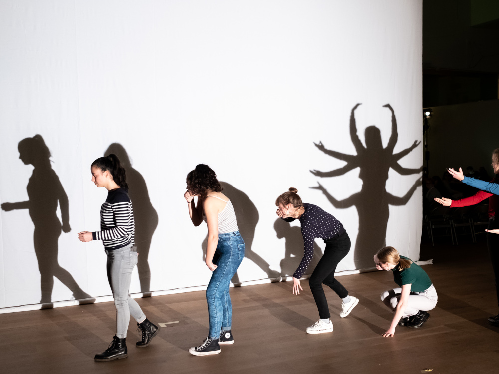 junge Saengerinnen bewegen sich vor einer Schattenwand