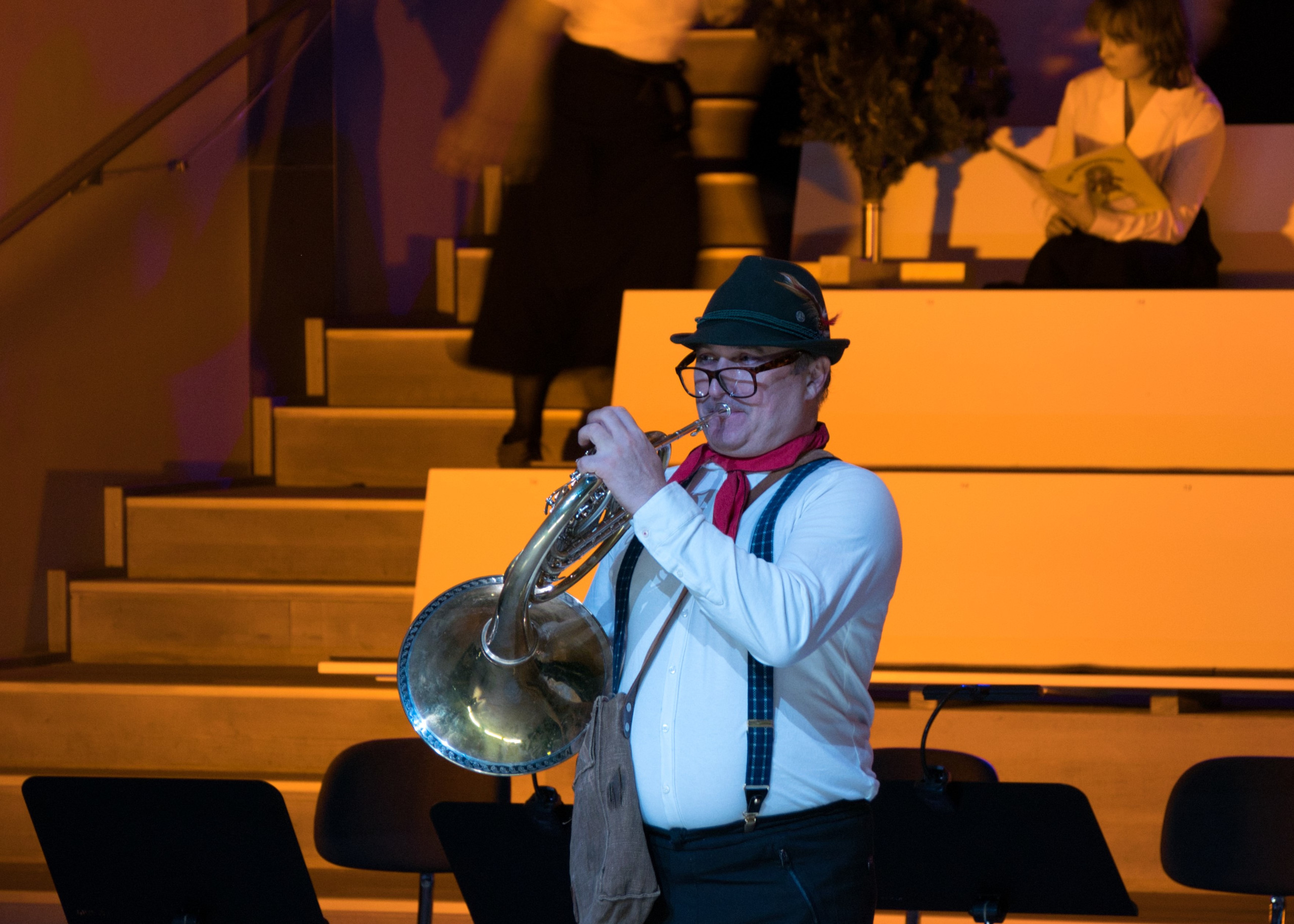 Ein Mann spielt Horn, er trägt eine grosse dunkle Brille und einen Jagdhut.