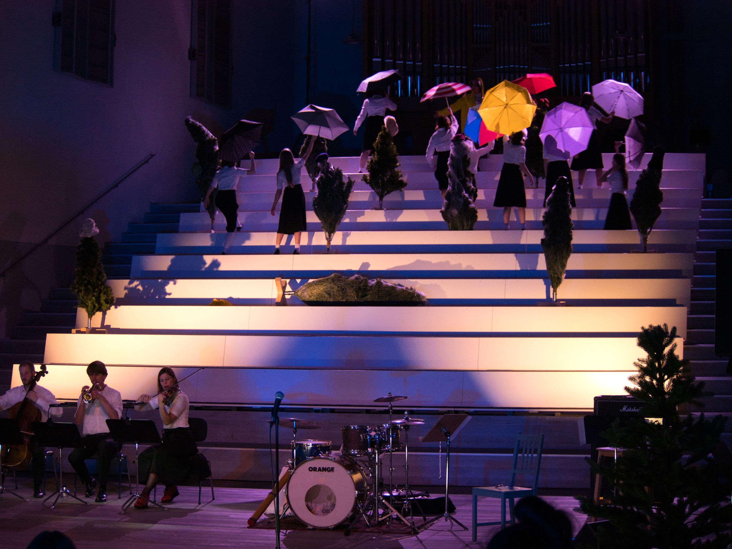 Personen tanzen auf der angeleuchteten Tribüne mit bunten Regenschirmen.