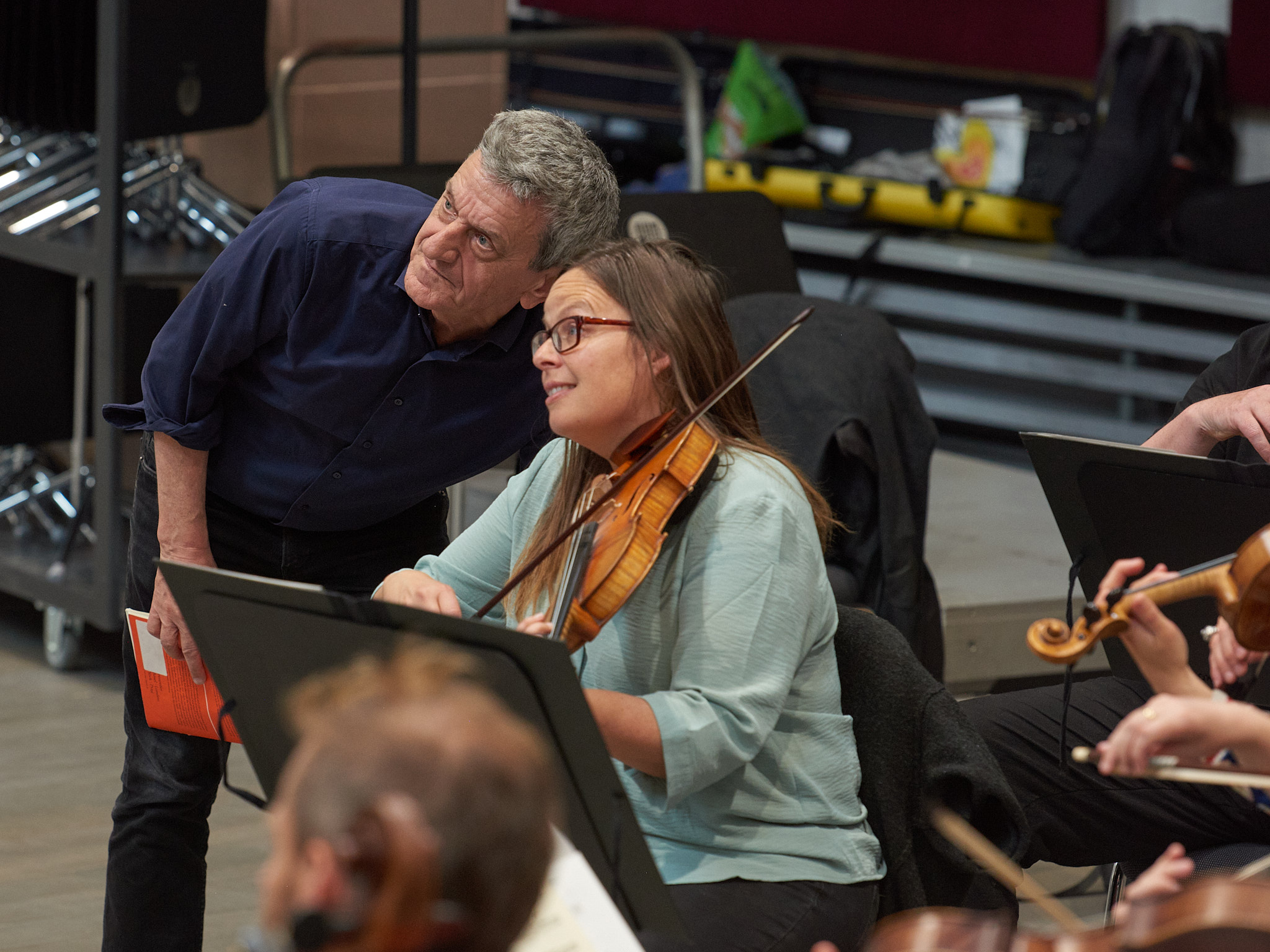 Im Fokus: eine nach links blickende, gespannte Geigerin und ein daneben stehender Herr.
