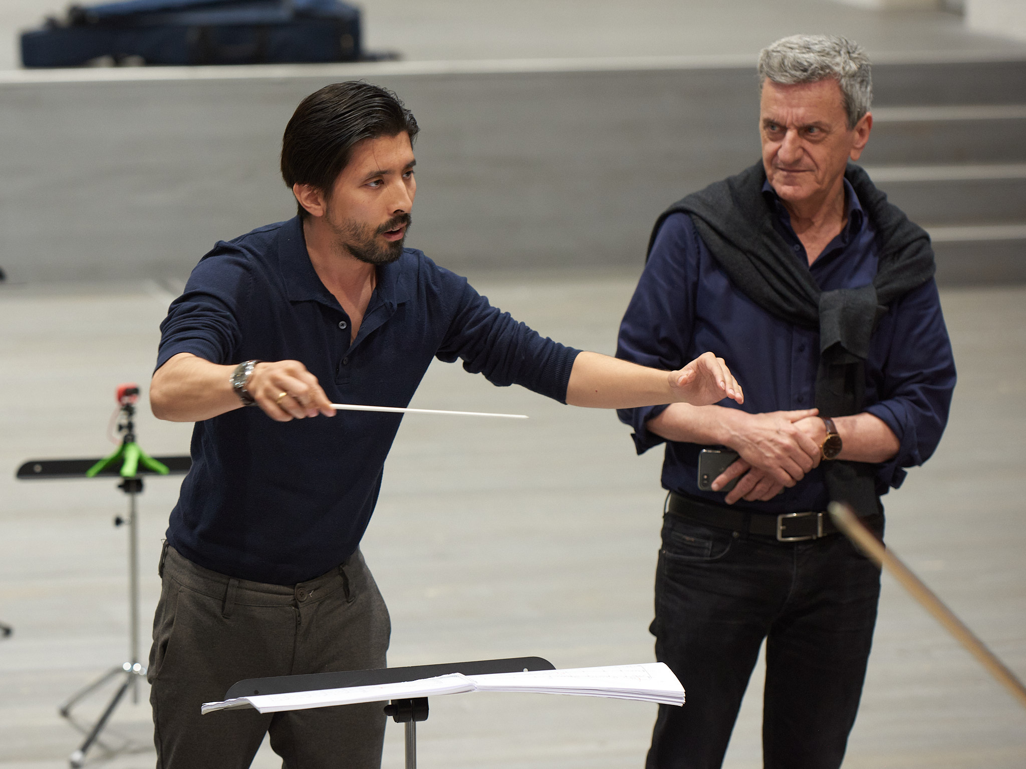 Junger Dirigent am Arbeiten, Mentor steht daneben und beobachtet ihn.