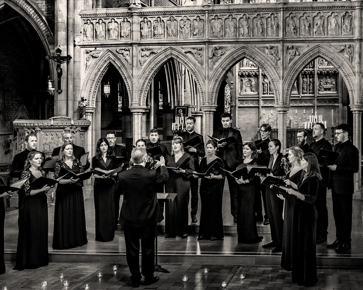 Chorbild des Tenebrae Choirs. Die Mitglieder des Chors stehen in einer prachtvollen Kathedrale und singen aus Notenheften.