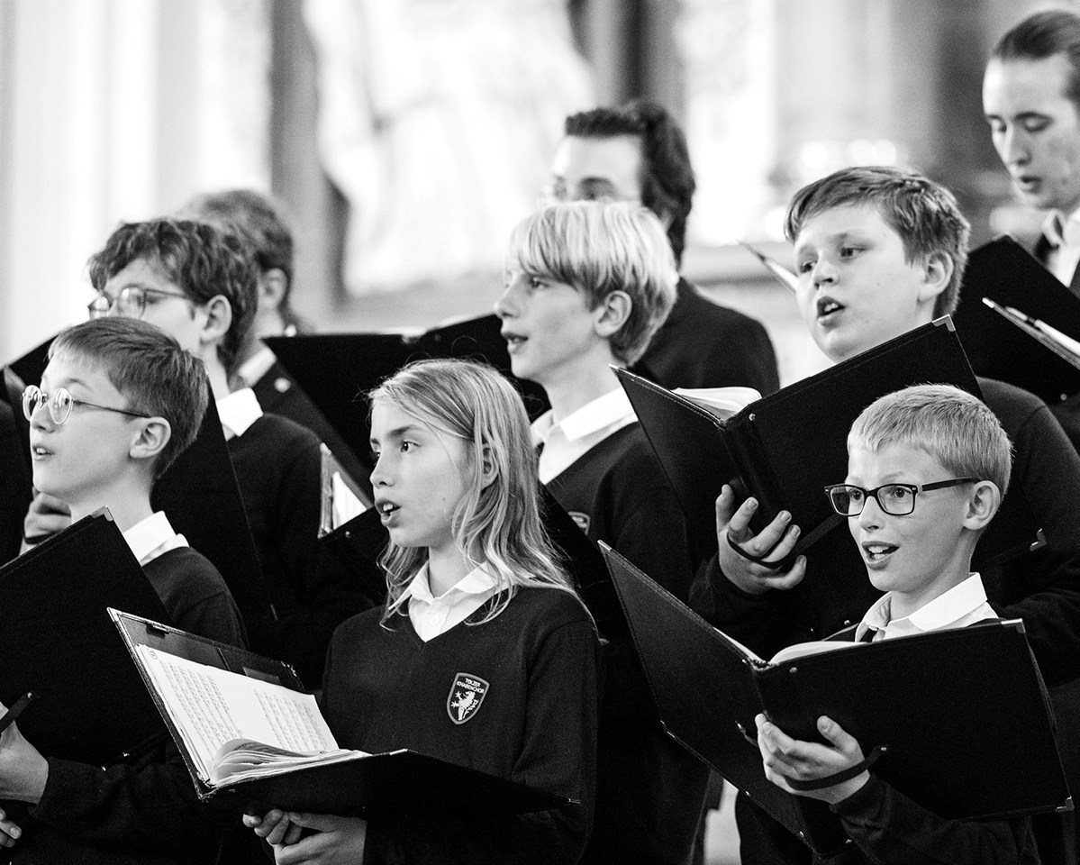 Konzertaufnahme des Toelzer Knabenchors. Die Choristen tragen ihre Notenmappen in der Hand und singen daraus.