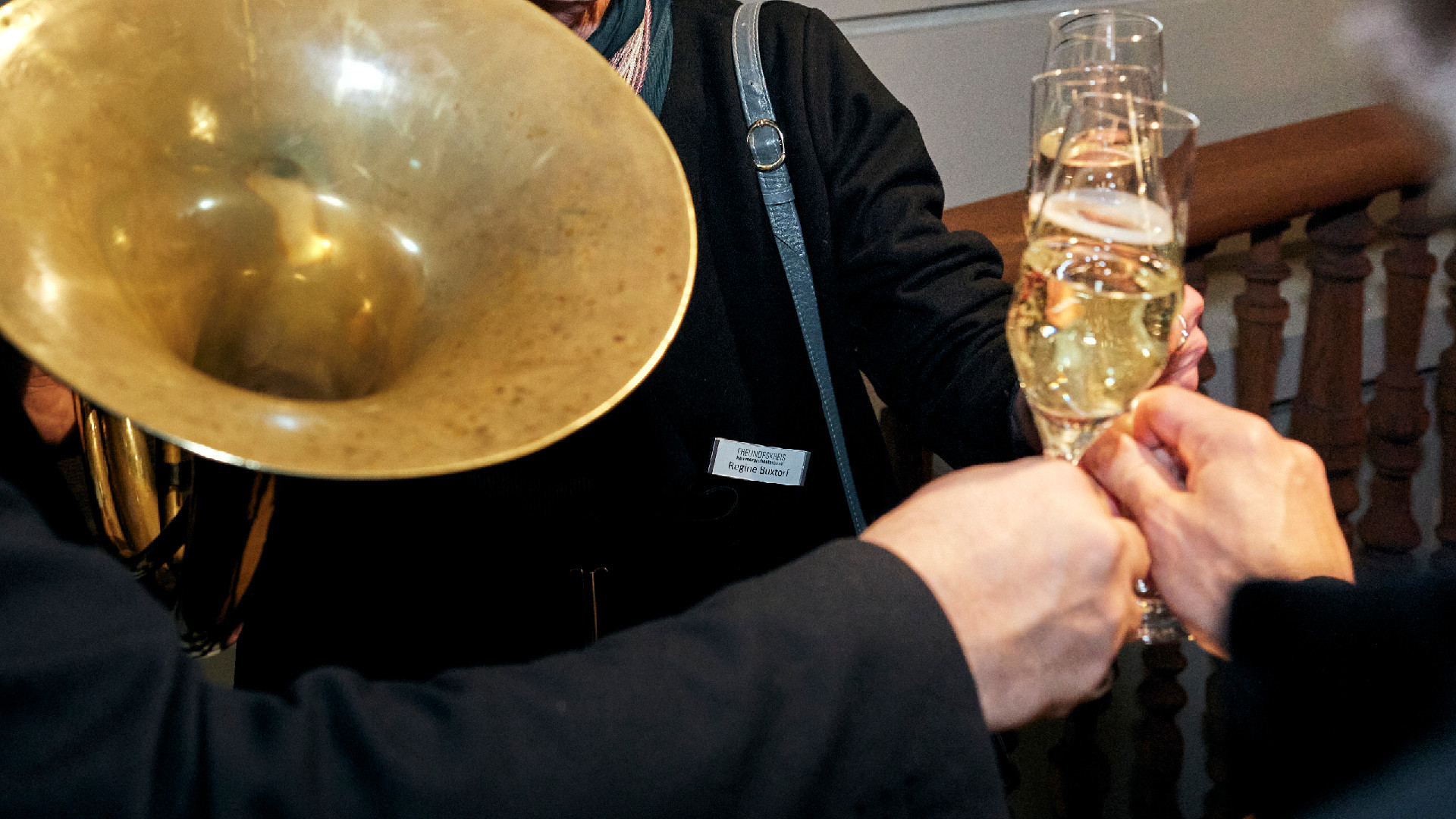 Drei Personen stossen mit Champagner an, eine Person hält dabei in der anderen Hand ein Horn.