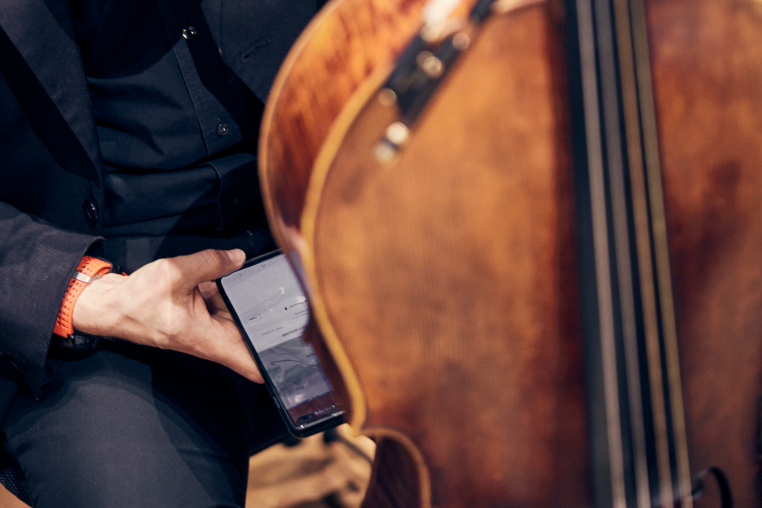 Detail picture: A cellist looks behind his instrument at his cell phone.