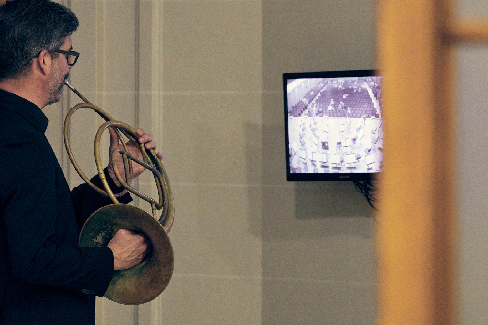 Ein Hornist spielt sich backstage warm und schaut dabei in den Konzertsaal hinein.