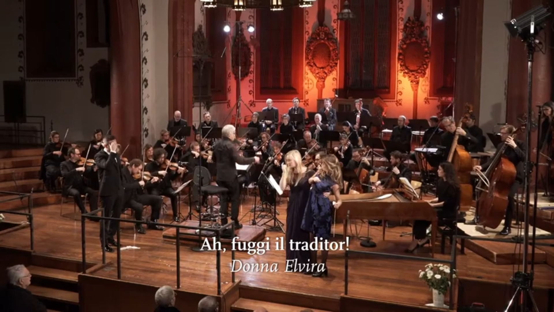 Das Kammerorchester Basel spielt in einer Kirche, im Vordergrund singen zwei Solistinnen. Eingeblendet ist der Titel "Ah, fuggi il traditor!".