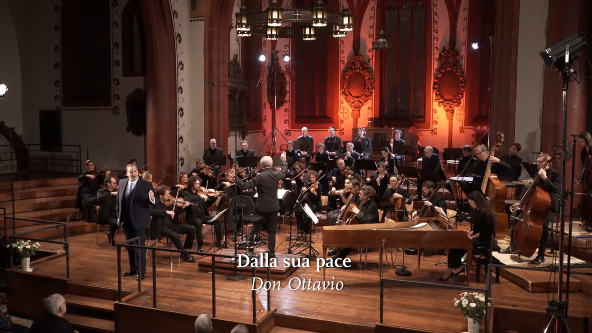 Das Kammerorchester Basel spielt in einer Kirche, im Vordergrund singt ein Solist. Eingeblendet ist der Titel "Dalla sua pace".