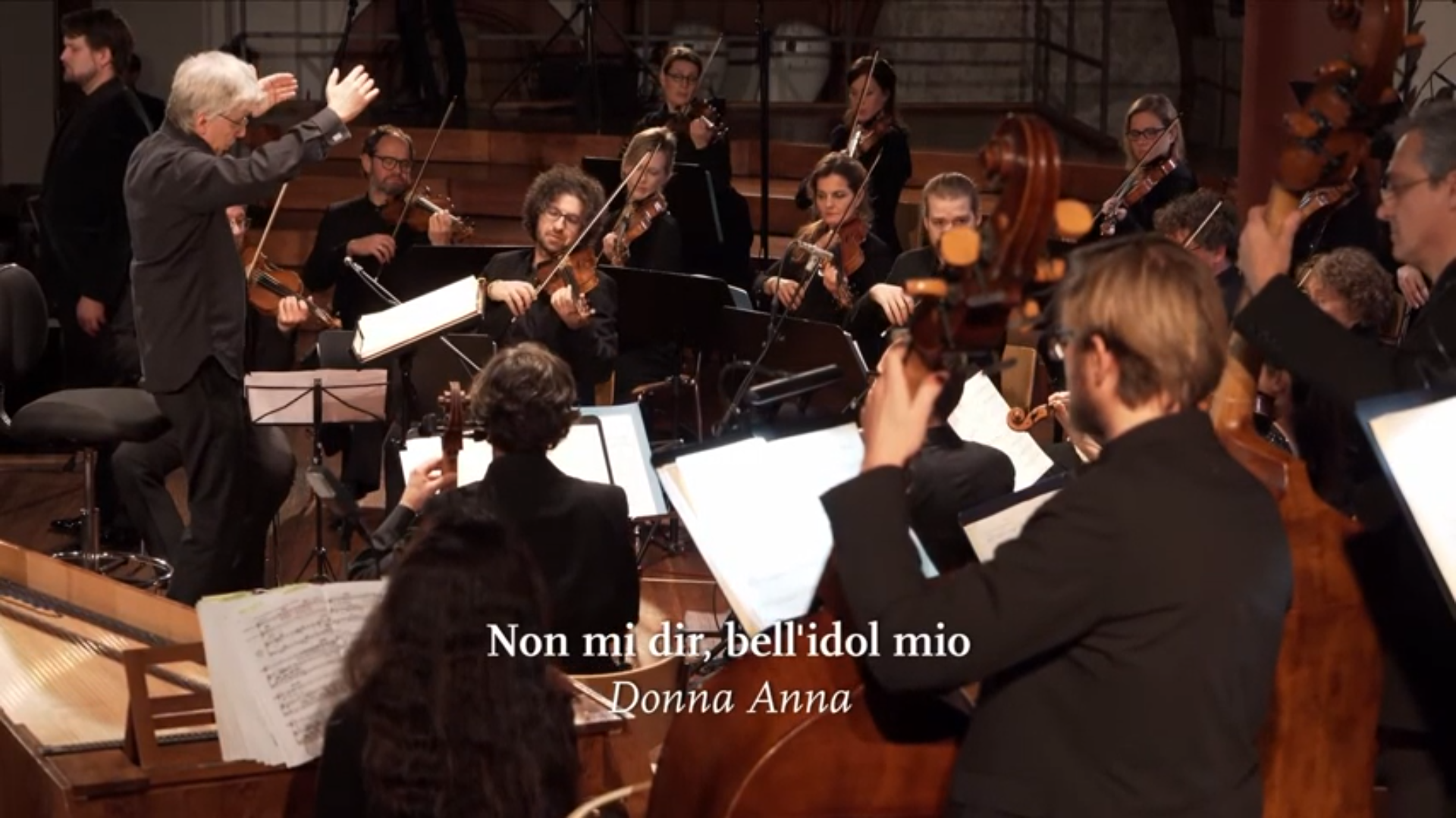 Das Kammerorchester Basel spielt in einer Kirche, der Dirigent Giovanni Antonini steht mit erhobenen Armen vor dem Orchester. Eingeblendet ist der Titel "Non mi dir, bell'idol mio".
