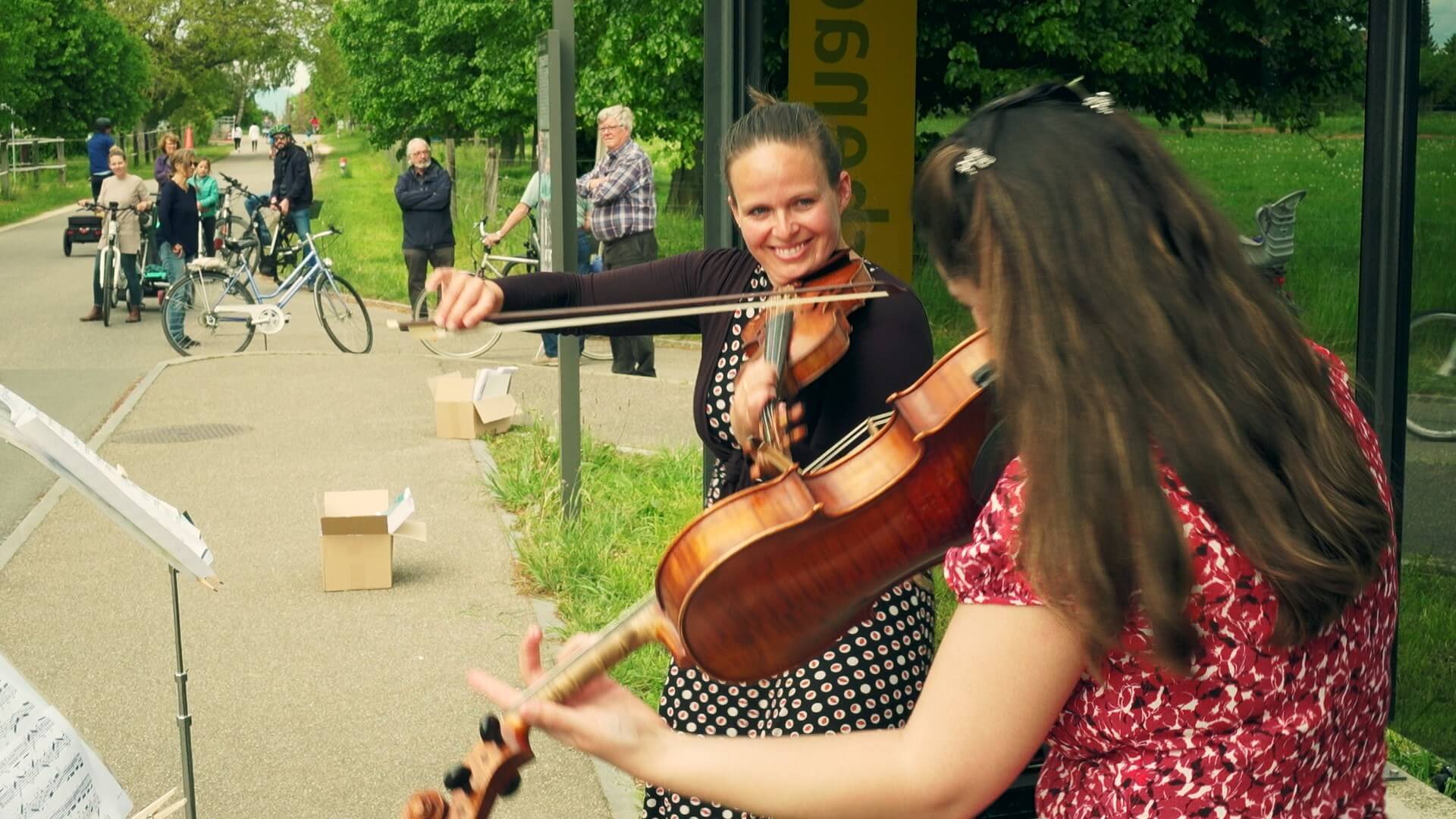 Eine Geigerin und eine Bratschistin spielen an einer Bushaltestelle.