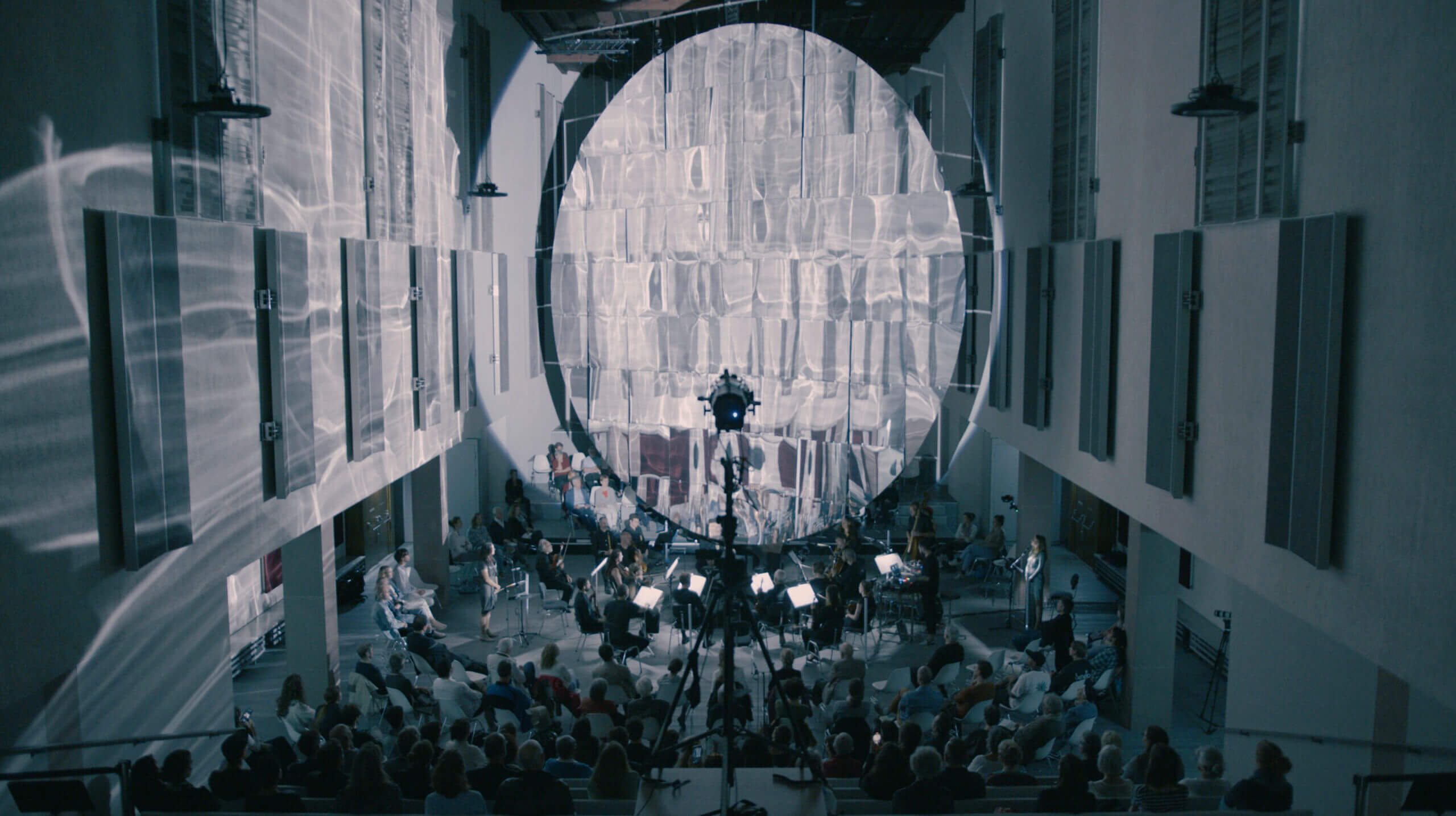 Schwarzweiss-Foto eines Konzerts. Muster werden an die Wand des Konzertsaals projiziert.