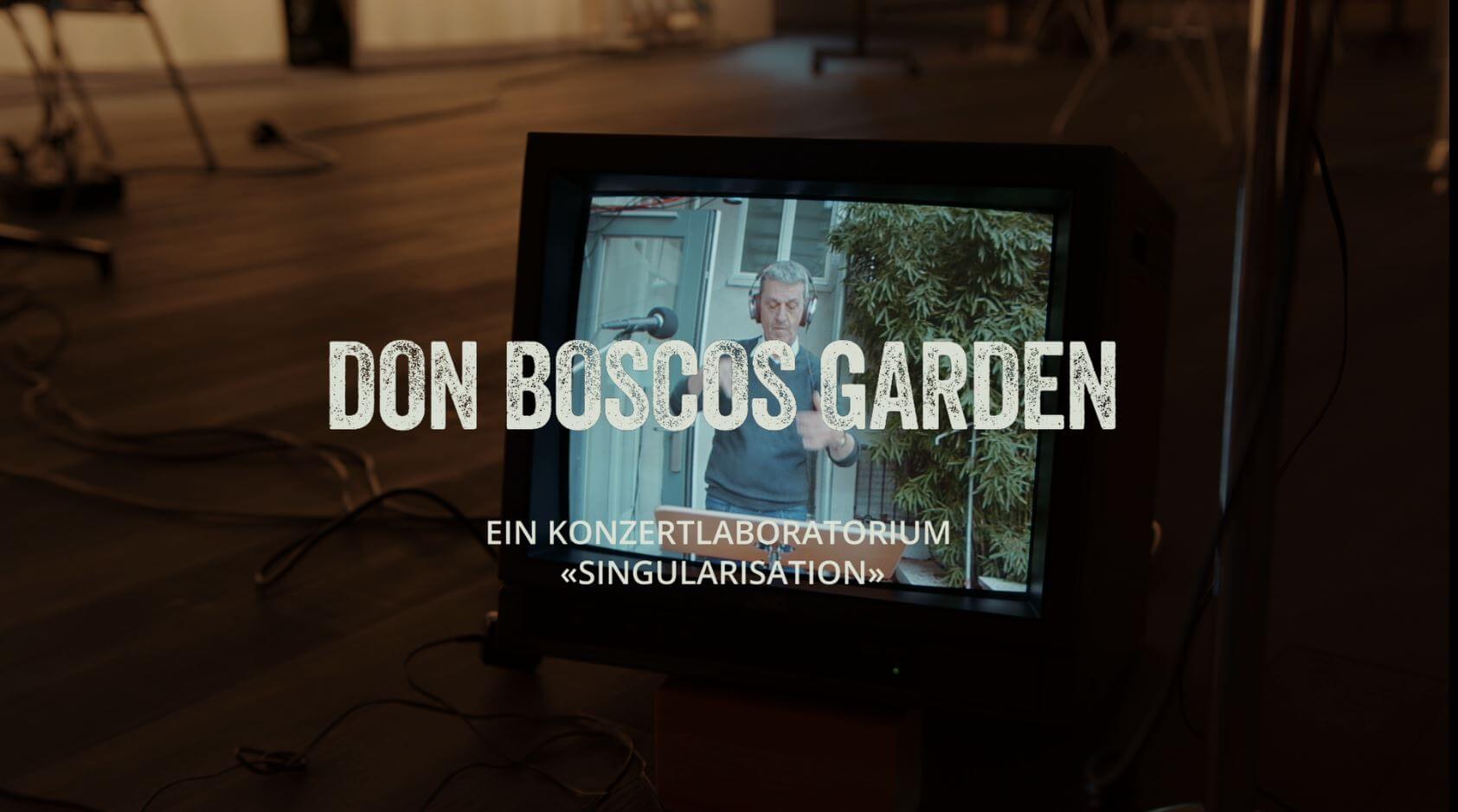 Fotografie eines Bildschirms, auf dem ein Dirigent mit aufgesetzten Kopfhörern zu sehen ist. Der Titel "Don Boscos Garden, ein Konzertlaboratorium Singularisation" wird eingeblendet.