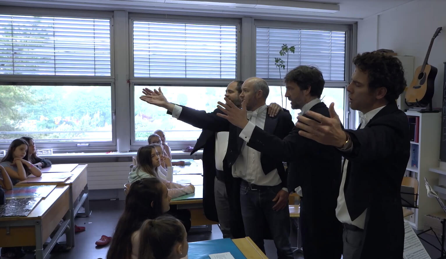 Vier Musiker Singen gekleidet im Frack vor einer Schulklasse im Klassenzimmer.