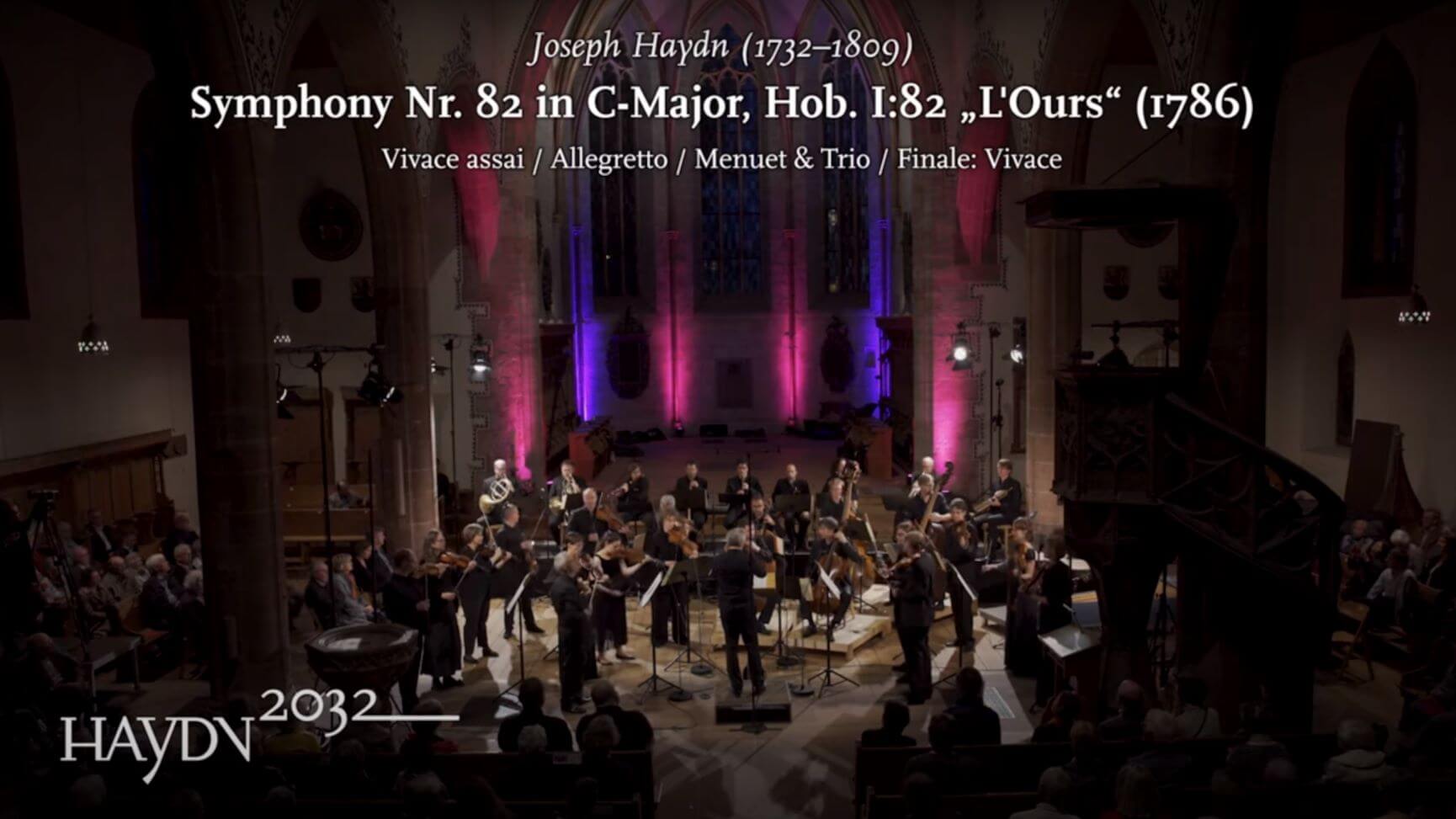 Das Kammerorchester Basel spielt in einer Kirche. Eingeblendet ist der Text: Joseph Haydn, Symphony No. 82 in C-Major, Hob. I:82 und das Logo des Projekts Haydn2032.