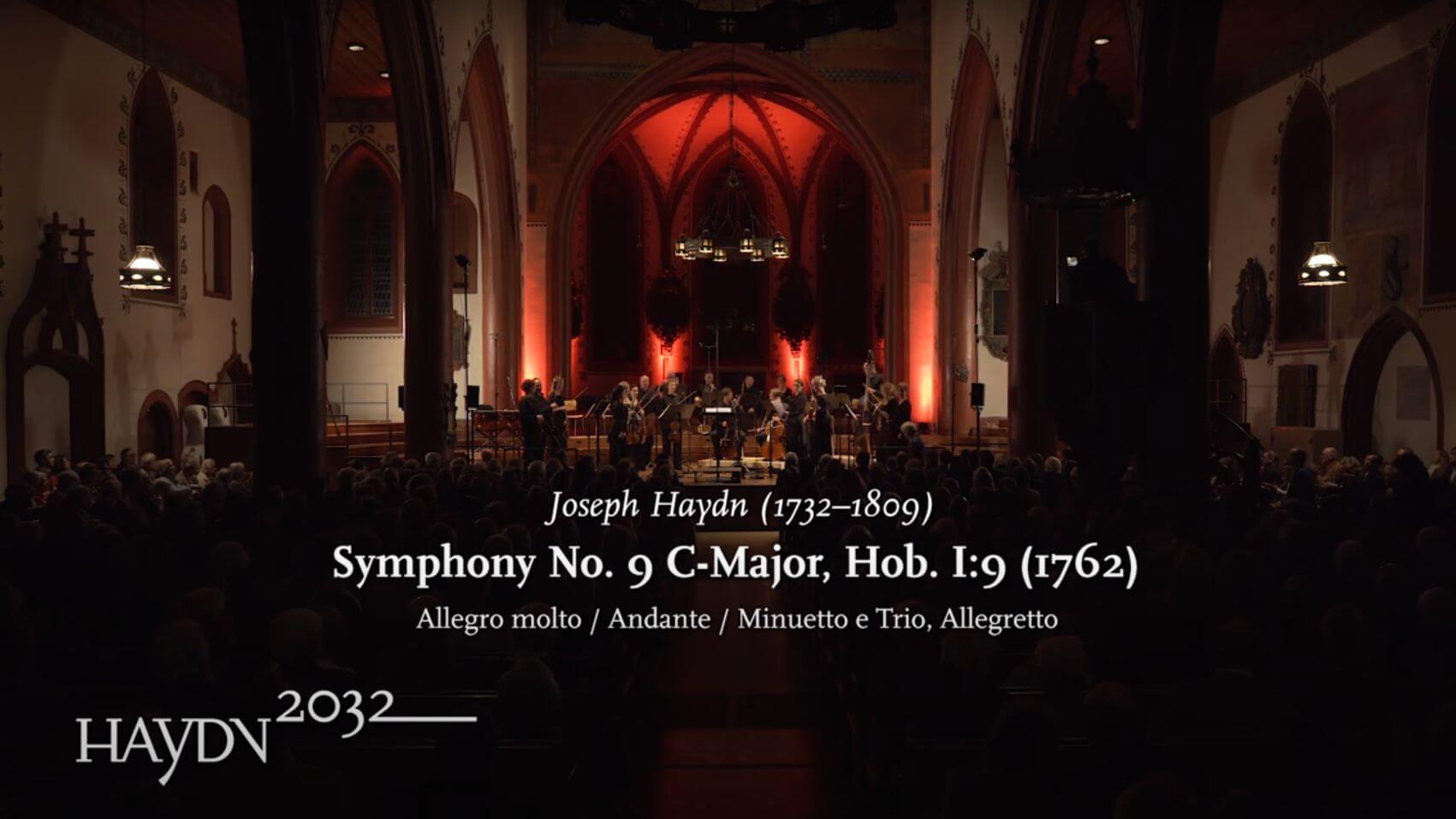 Das Kammerorchester Basel spielt in einer Kirche. Eingeblendet ist der Text: Joseph Haydn, Symphony No. 9 in D-Major, Hob. I:9 und das Logo des Projekts Haydn2032.