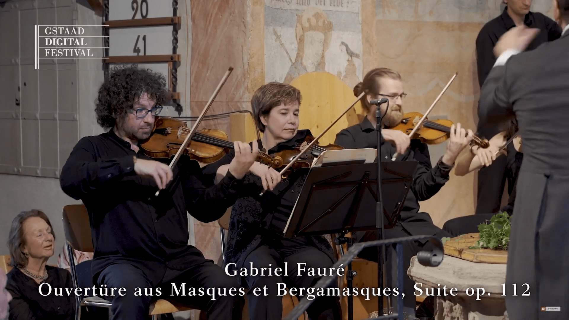 Violinist:innen des Orchesters sind zu sehen. Eingeblendet ist der Text: Gabriel Fauré, Ouvertüre aus Masques et Bergamasques, Suite op. 112.