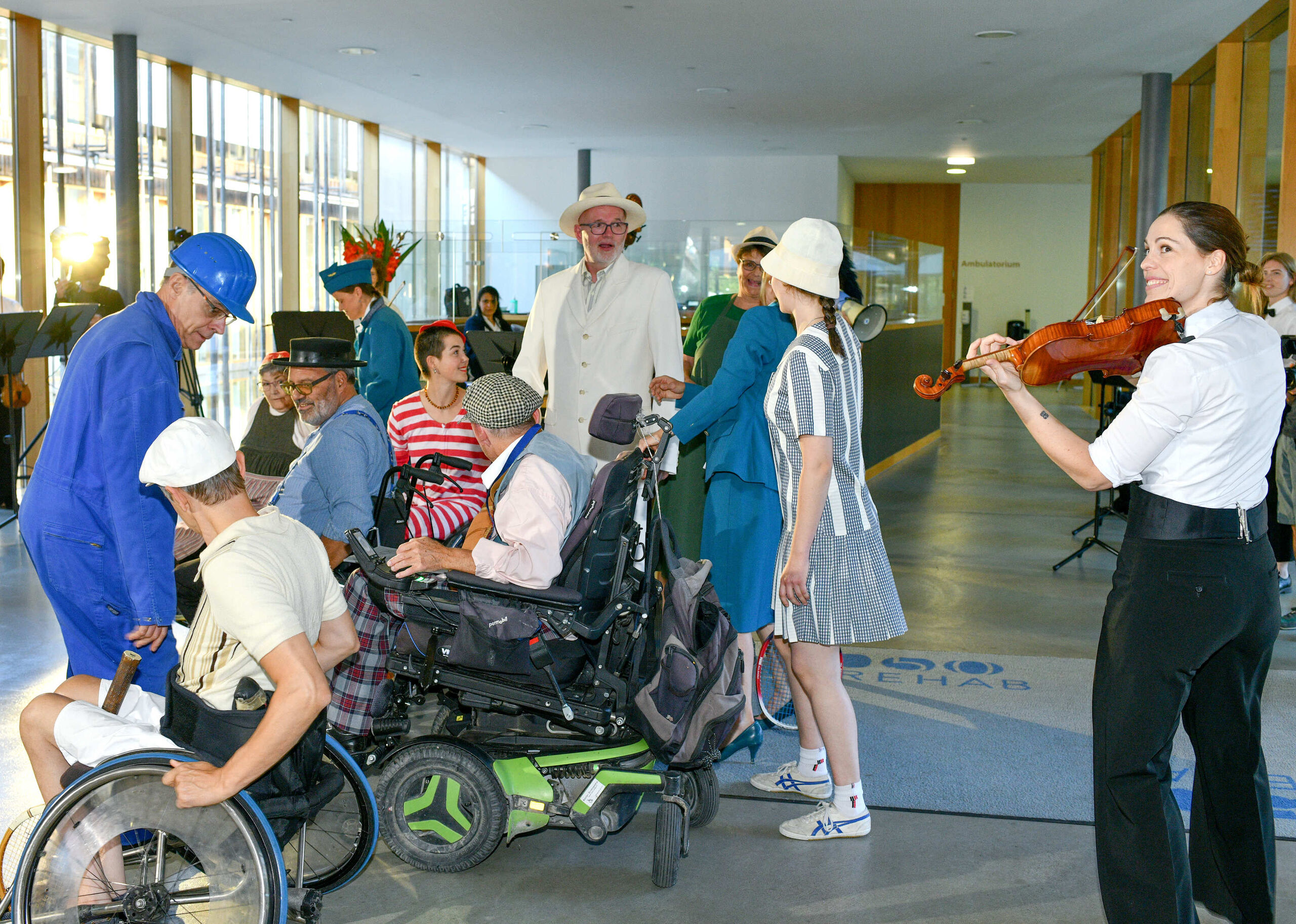 Kostümierte Darsteller:innen mit und ohne Rollstuhl, daneben eine Geigerin.