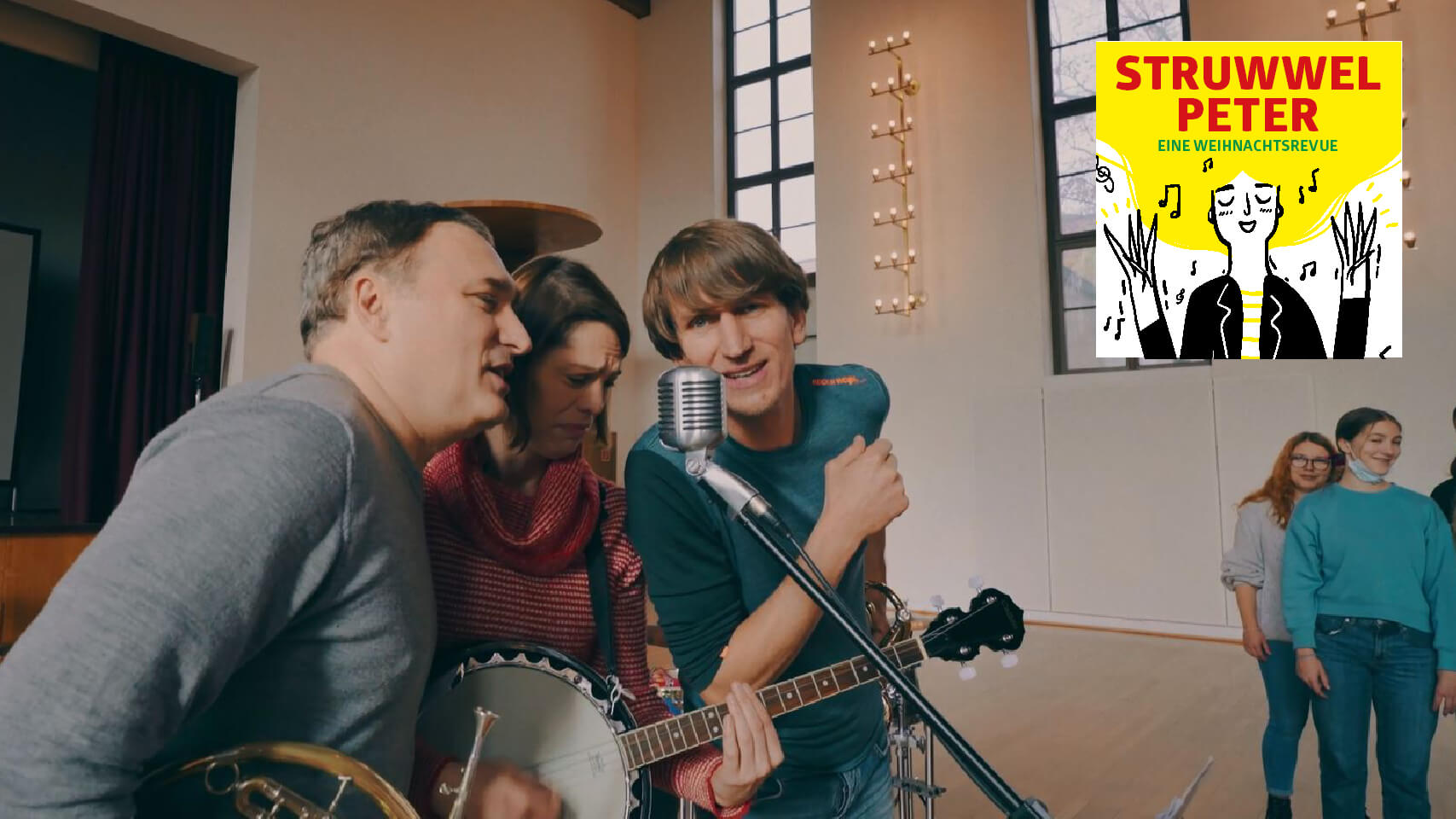 Drei Musiker:innen stehen gemeinsam vor einem Mikrofon. Oben rechts im Bild eingeblendet ein Logo mit einer Zeichnung von Struwwelpeter.