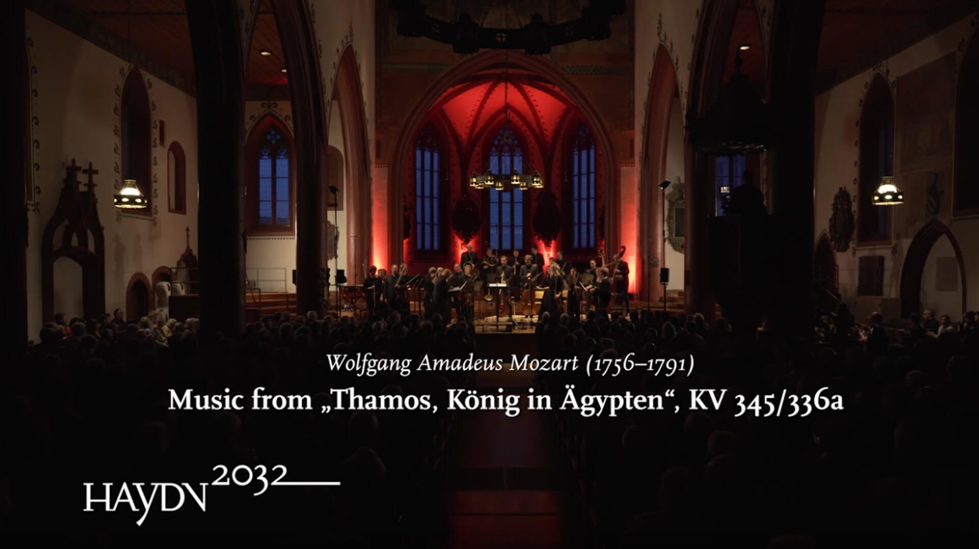 Das Kammerorchester Basel spielt in einer Kirche. Eingeblendet ist der Text: Wolfgang Amadeus Mozart, Musik from "Thamos, König in Ägypten", KV 345/336a und das Logo des Projekts Haydn2032.