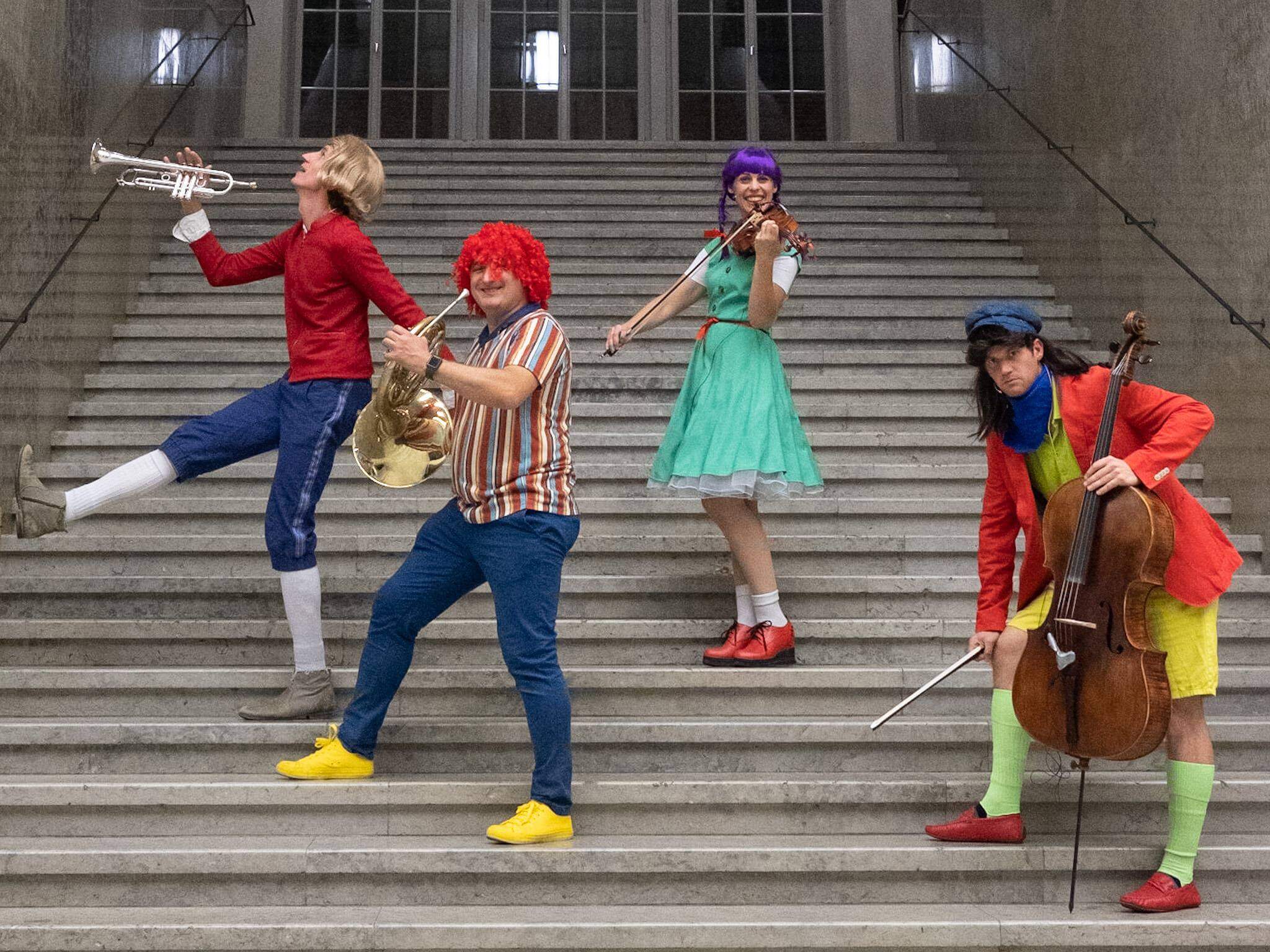 Vier Musiker:innen stehen verkleidet und mit ihren Instrumenten auf einer Treppe.