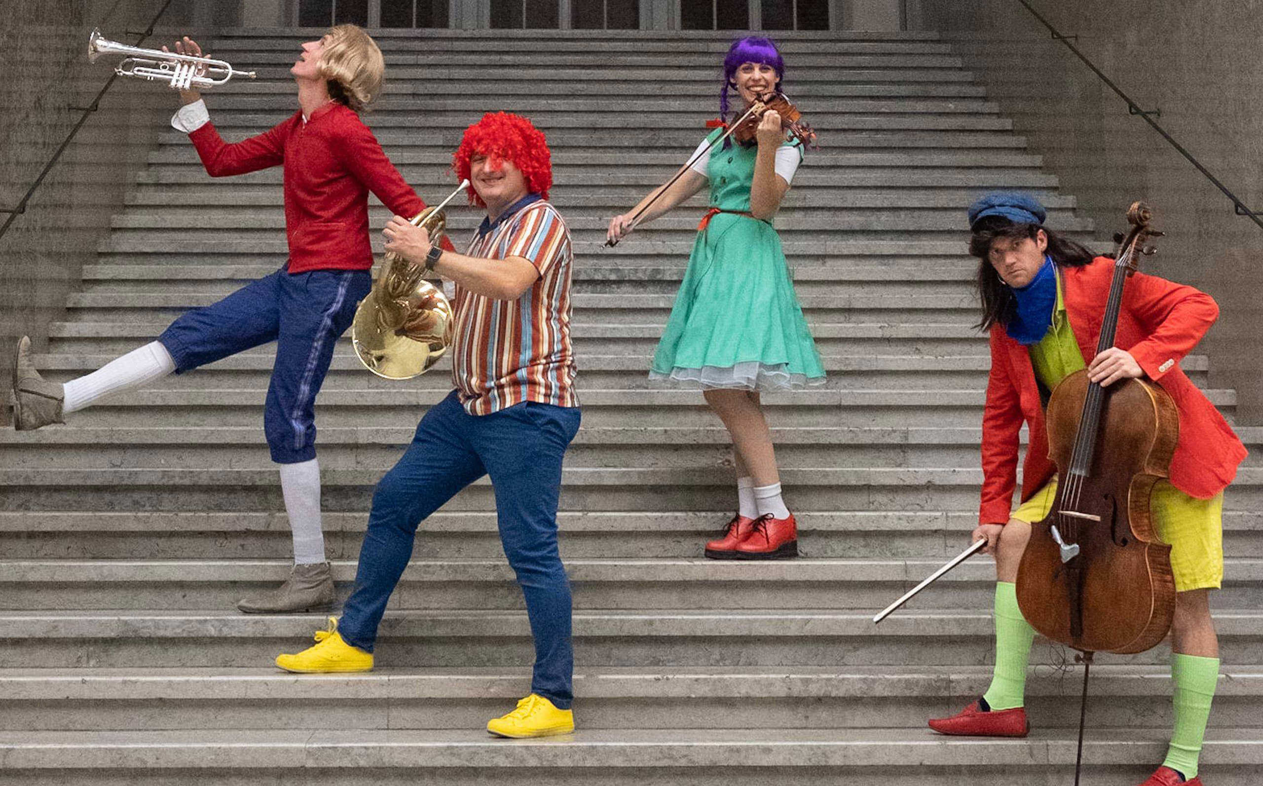 Vier Musiker:innen stehen verkleidet und mit ihren Instrumenten auf einer Treppe.